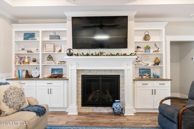 living room with a fireplace, crown molding, built in shelves, and wood finished floors