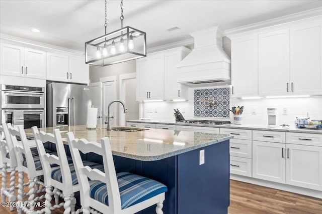 kitchen with backsplash, appliances with stainless steel finishes, premium range hood, and a sink