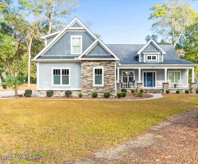 craftsman house featuring stone siding, covered porch, board and batten siding, and a front yard