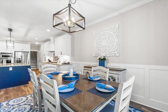 dining space featuring a wainscoted wall, ornamental molding, stairs, light wood-style floors, and a chandelier