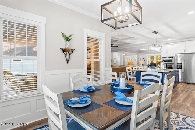 dining area featuring a wainscoted wall, light wood-style flooring, an inviting chandelier, crown molding, and a decorative wall