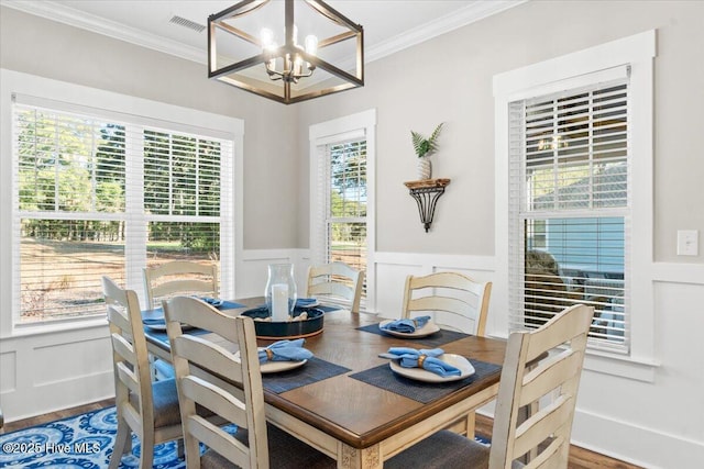 dining area featuring a wainscoted wall, a notable chandelier, wood finished floors, and crown molding