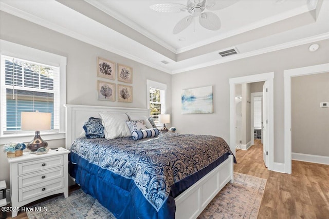 bedroom featuring visible vents, baseboards, a tray ceiling, ornamental molding, and wood finished floors