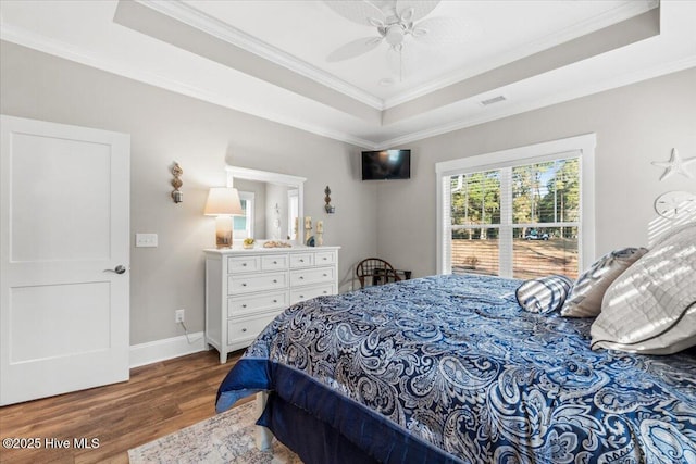 bedroom featuring a tray ceiling, crown molding, wood finished floors, and baseboards