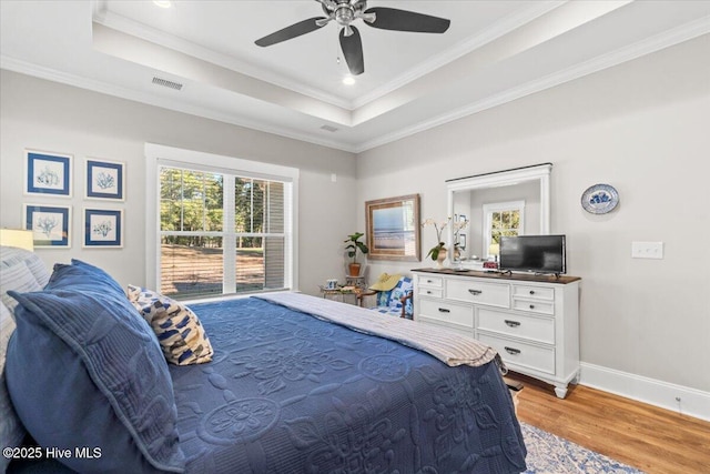 bedroom featuring a tray ceiling, light wood-style flooring, crown molding, and baseboards