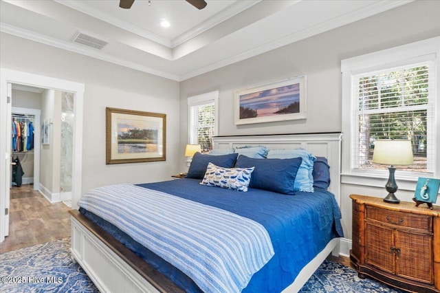 bedroom featuring visible vents, a tray ceiling, wood finished floors, crown molding, and ceiling fan