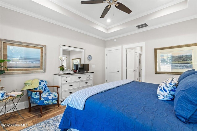 bedroom featuring visible vents, ornamental molding, wood finished floors, baseboards, and a raised ceiling