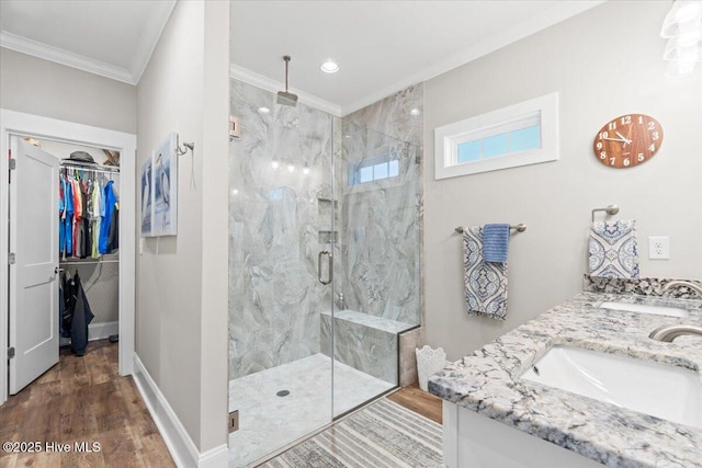 bathroom featuring wood finished floors, a marble finish shower, ornamental molding, a sink, and a walk in closet