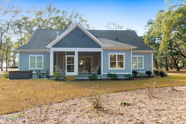 rear view of house featuring roof with shingles, a sunroom, and a hot tub