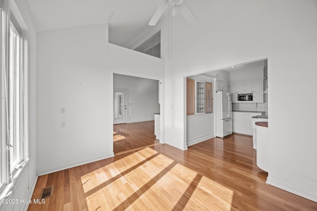 unfurnished living room featuring a ceiling fan, baseboards, visible vents, and light wood finished floors