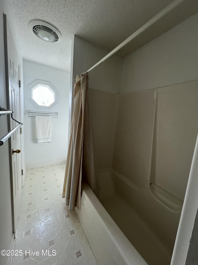 bathroom with shower / bath combination with curtain and a textured ceiling