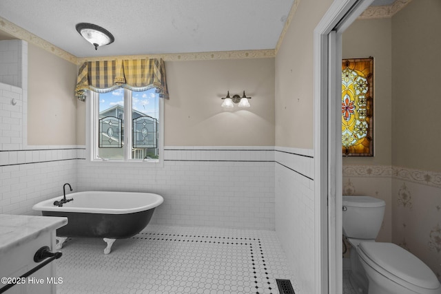 bathroom with toilet, tile walls, and wainscoting