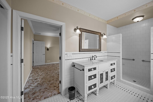bathroom featuring crown molding, tile walls, a tile shower, vanity, and a wainscoted wall