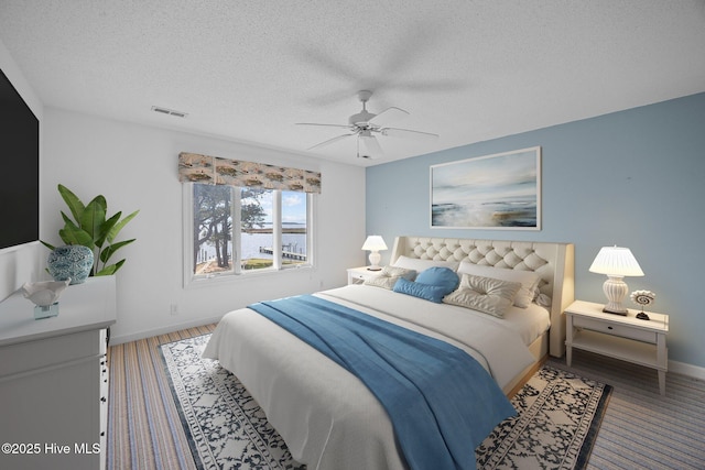 bedroom with a ceiling fan, a textured ceiling, visible vents, wood finished floors, and baseboards