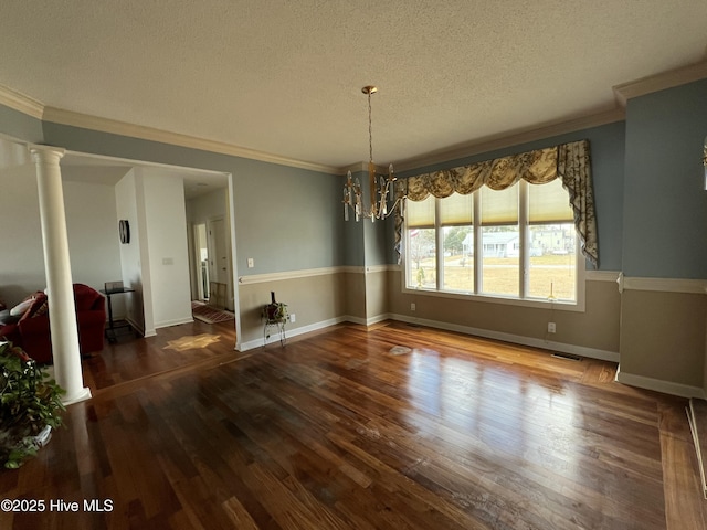 unfurnished dining area featuring a textured ceiling, dark hardwood / wood-style floors, ornamental molding, a chandelier, and decorative columns