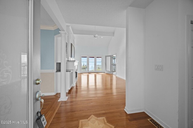 corridor with visible vents, baseboards, wood finished floors, ornate columns, and vaulted ceiling