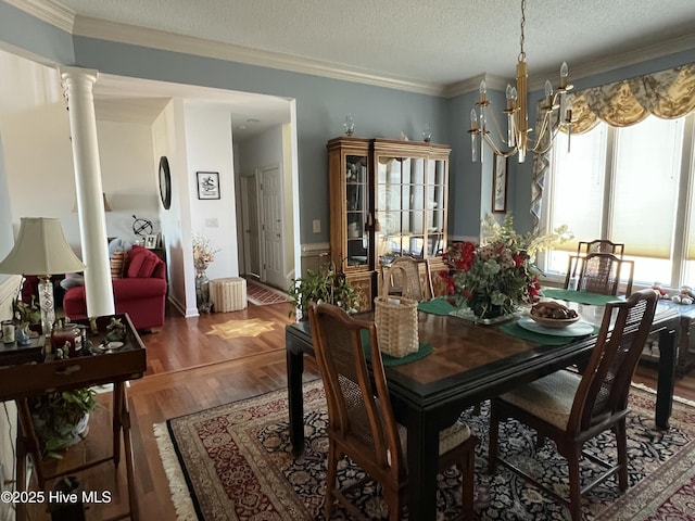 dining space featuring a notable chandelier, hardwood / wood-style floors, a textured ceiling, decorative columns, and ornamental molding