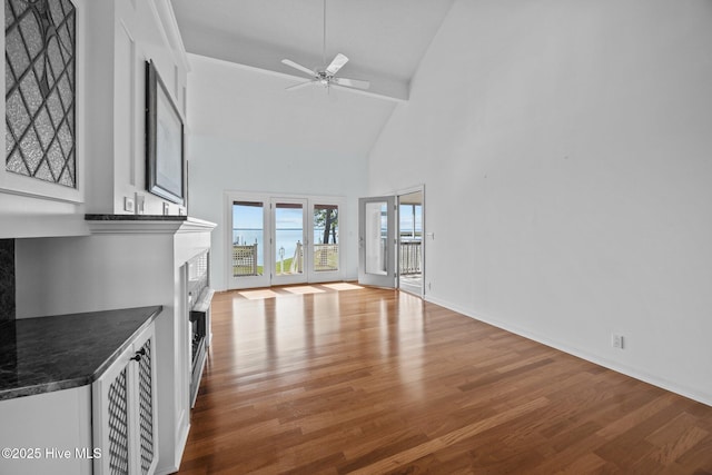 unfurnished living room featuring ceiling fan, high vaulted ceiling, baseboards, wood finished floors, and a high end fireplace