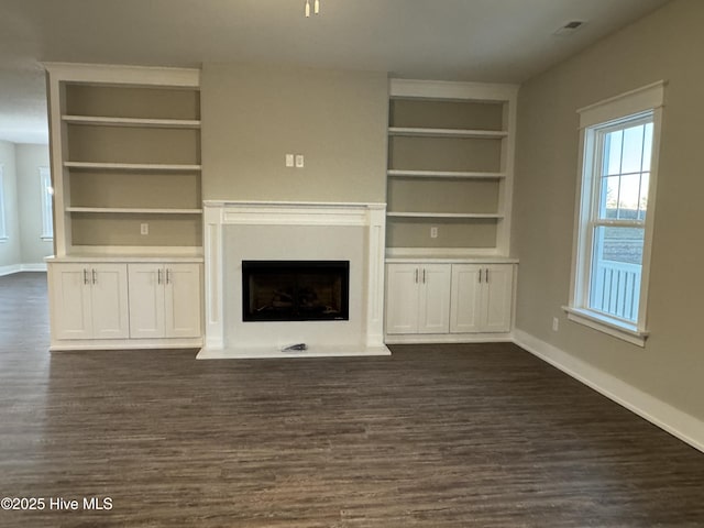 unfurnished living room with dark wood-type flooring and built in shelves