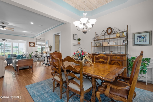 dining space with a tray ceiling, ornamental molding, ceiling fan with notable chandelier, and hardwood / wood-style flooring