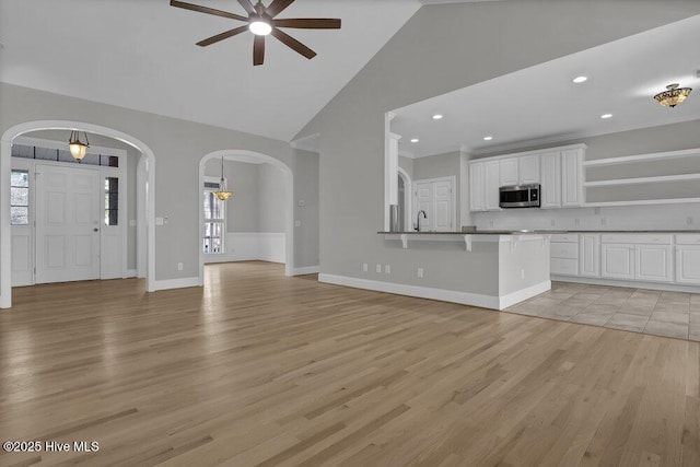 unfurnished living room featuring ceiling fan, light wood-type flooring, sink, and a towering ceiling