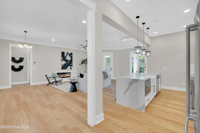 kitchen with decorative light fixtures, ornamental molding, ceiling fan, light hardwood / wood-style floors, and light stone countertops