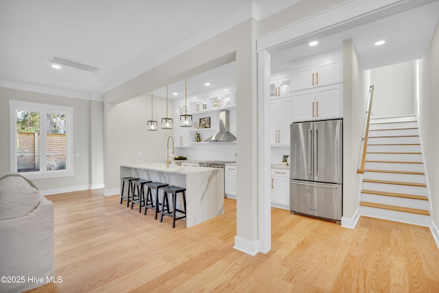 kitchen featuring pendant lighting, stainless steel appliances, wall chimney range hood, and white cabinets