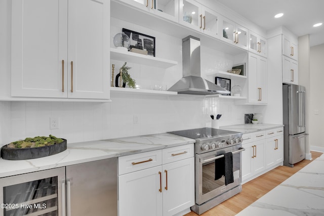 kitchen featuring light stone counters, wall chimney range hood, stainless steel appliances, beverage cooler, and white cabinets