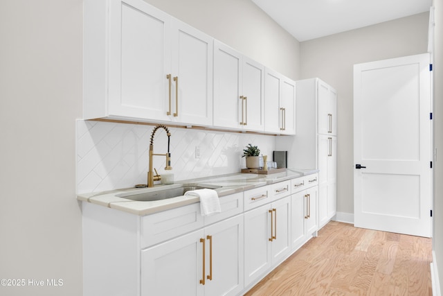 kitchen with sink, tasteful backsplash, light hardwood / wood-style flooring, light stone countertops, and white cabinets