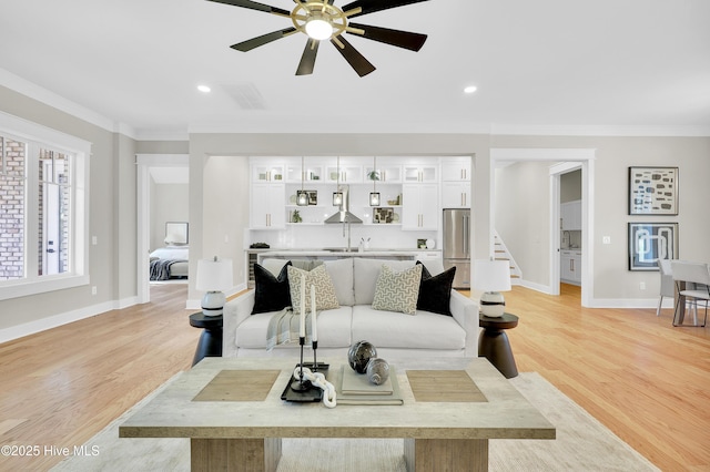 living room featuring sink, ornamental molding, light hardwood / wood-style floors, and ceiling fan