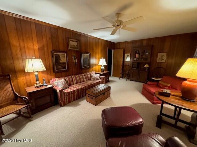 living room with ceiling fan, wood walls, and light colored carpet