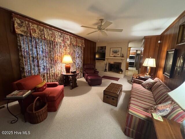 living room with ceiling fan, carpet floors, a fireplace, and wooden walls