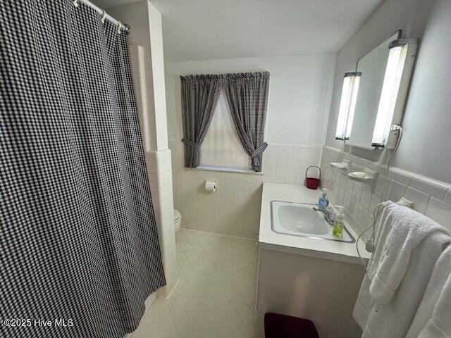 bathroom featuring vanity, curtained shower, toilet, and tile walls