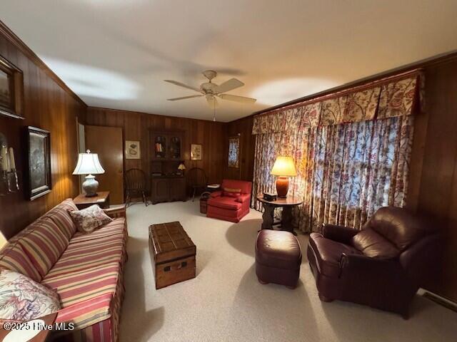 living room with ceiling fan, wood walls, carpet floors, and ornamental molding