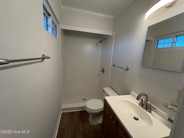 bathroom with a tile shower, crown molding, hardwood / wood-style floors, toilet, and vanity