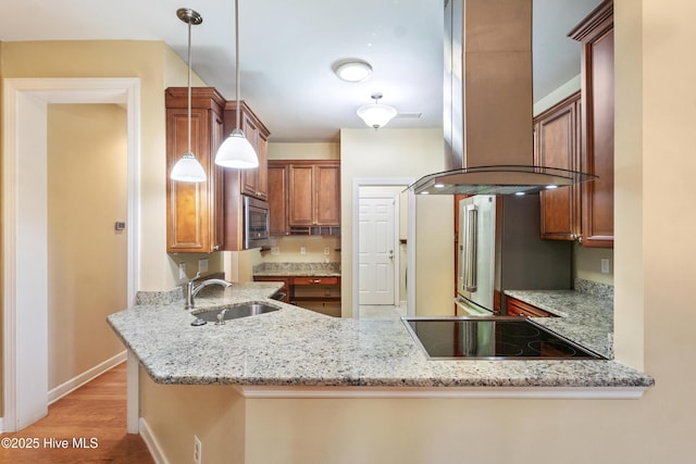 kitchen with decorative light fixtures, sink, light stone counters, and kitchen peninsula