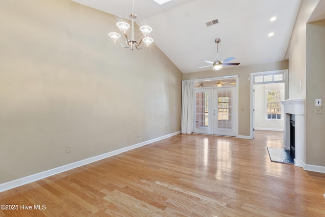 unfurnished living room with ceiling fan with notable chandelier, high vaulted ceiling, french doors, and light wood-type flooring