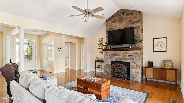 living room with wood-type flooring, ceiling fan, vaulted ceiling, and a stone fireplace