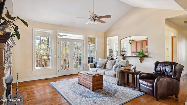 living room featuring ceiling fan, french doors, high vaulted ceiling, a fireplace, and light hardwood / wood-style flooring