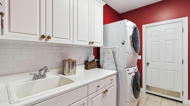 clothes washing area featuring sink, stacked washing maching and dryer, light tile patterned flooring, and cabinets