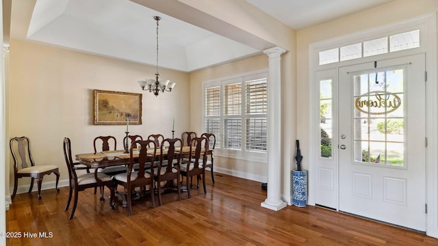 dining area featuring decorative columns, dark wood-type flooring, a raised ceiling, and a notable chandelier