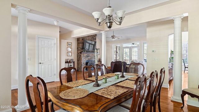 dining room with ceiling fan with notable chandelier, hardwood / wood-style floors, and a stone fireplace