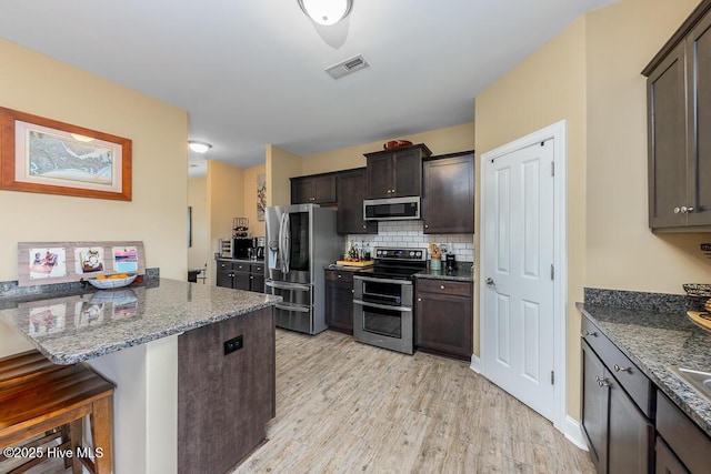 kitchen featuring a breakfast bar area, a peninsula, visible vents, light wood-style floors, and appliances with stainless steel finishes