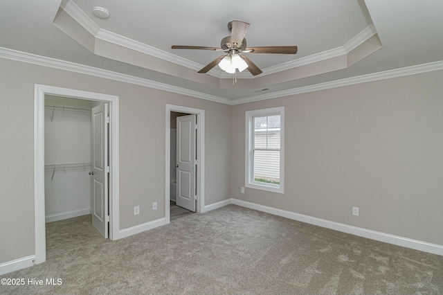 unfurnished bedroom featuring light carpet, a raised ceiling, a spacious closet, and ceiling fan