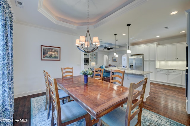 dining room with ornamental molding, dark wood-type flooring, ceiling fan, and a tray ceiling