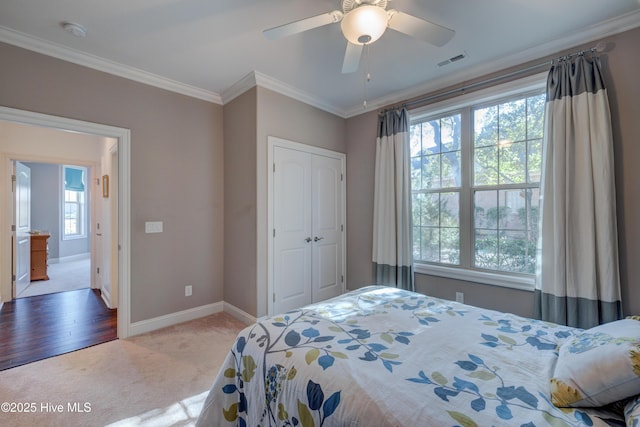 carpeted bedroom featuring multiple windows, crown molding, a closet, and ceiling fan