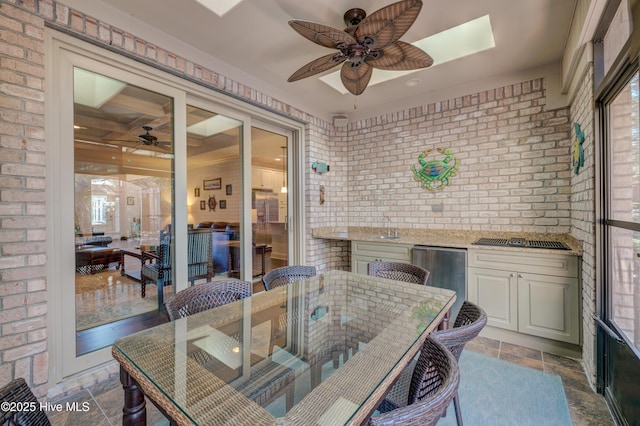 dining area with sink, a skylight, ceiling fan, and brick wall