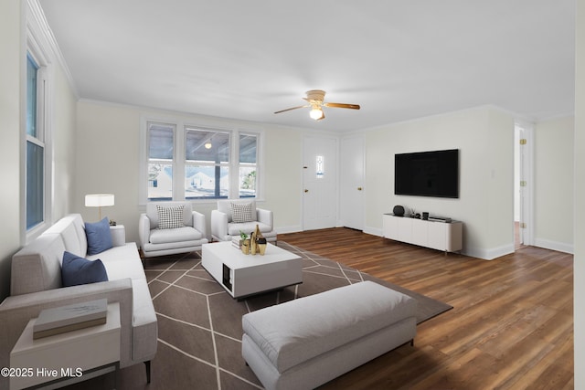 living area with ornamental molding, dark wood finished floors, baseboards, and a ceiling fan