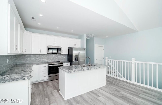 kitchen with light stone counters, white cabinetry, stainless steel appliances, and an island with sink