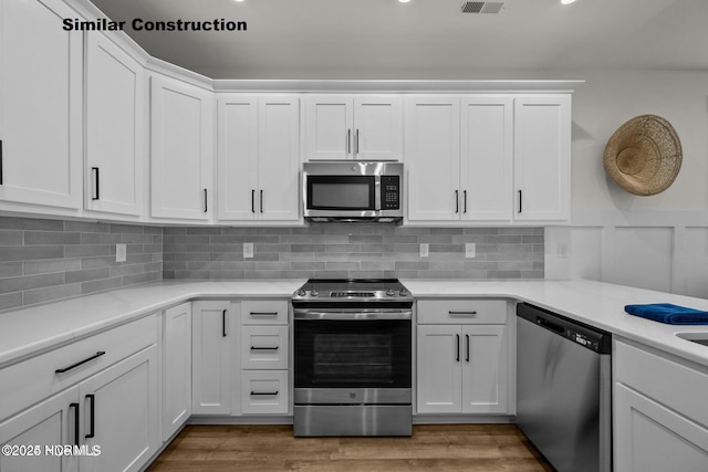 kitchen with decorative backsplash, appliances with stainless steel finishes, white cabinetry, and hardwood / wood-style floors